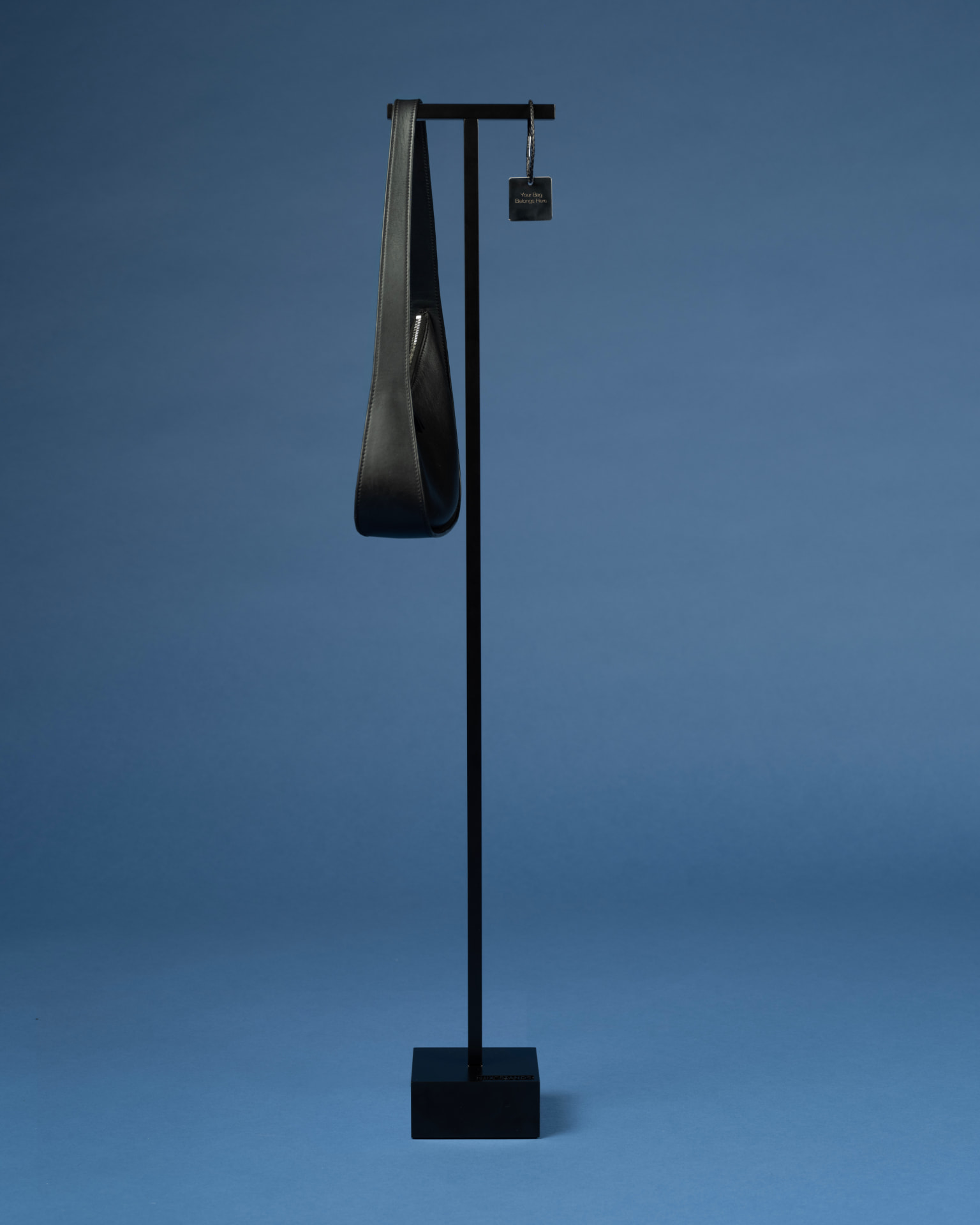 Full-length Luxestands stand presenting a black leather bag against a slate-blue backdrop.